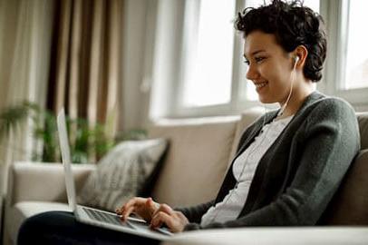 A younger woman with headphones in on her laptop